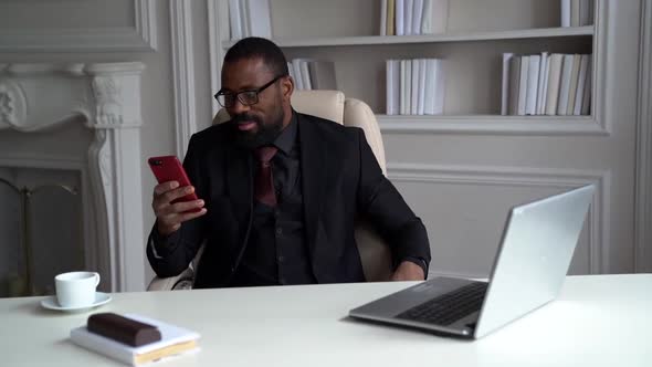 African-American Bearded Man in a Black Suit, Shirt, Stylish Glasses. A Businessman Is Working on a