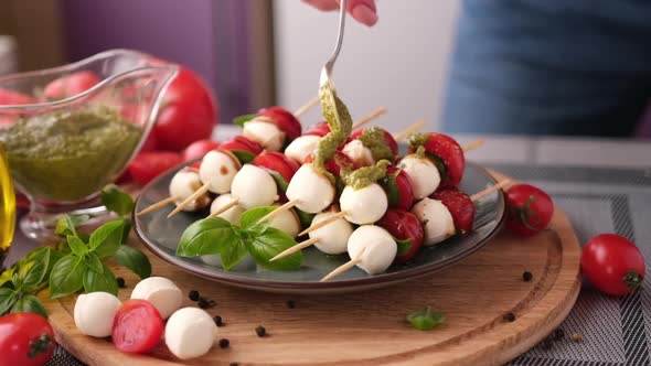 Pouring Pesto Sauce on Caprese Canapes with Cherry Tomatoes and Mozzarella Cheese Balls