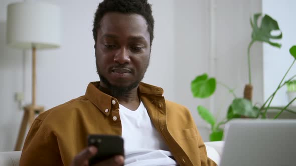 African Man Talking on Phone with Computer in Home Interior Spbas