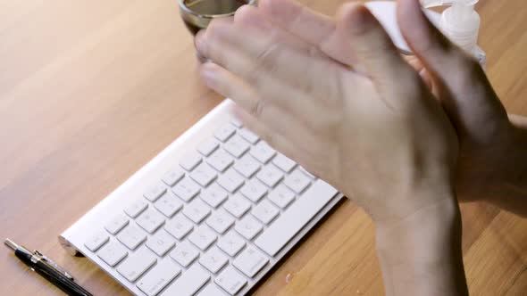 Person cleaning her hands with sanitizer at work above a laptop computer at a small office during th