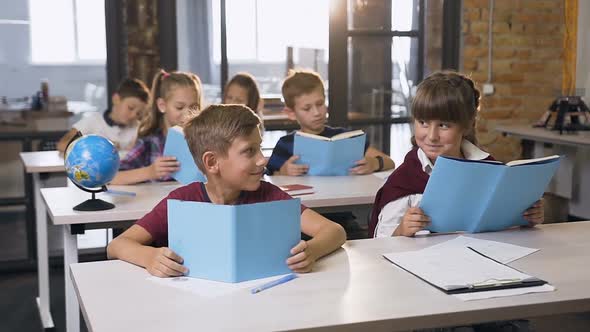 Lovely Boy and Girl of Elementary School Sitting at the Desk Looking Each other Smiling