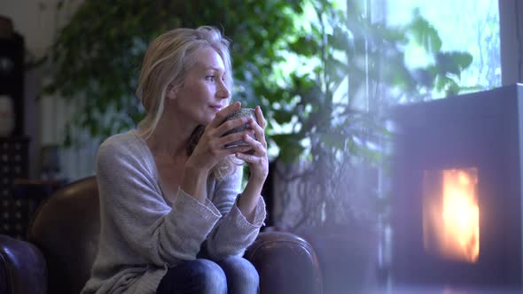 Mature woman drinking coffee in front of the fireplace