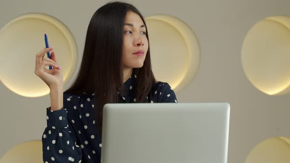 Thoughtful Business Asian Woman Working at a Computer Smiling and Looking Into the Distance Thinking