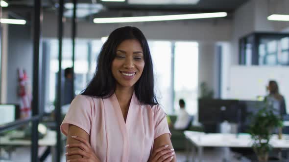 Portrait of mixed race businesswoman standing in office with arms crossed smiling to camera