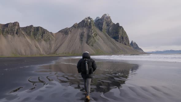 Hiker Walking Along Black Sand Beach Towards Vestrahorn Mountain