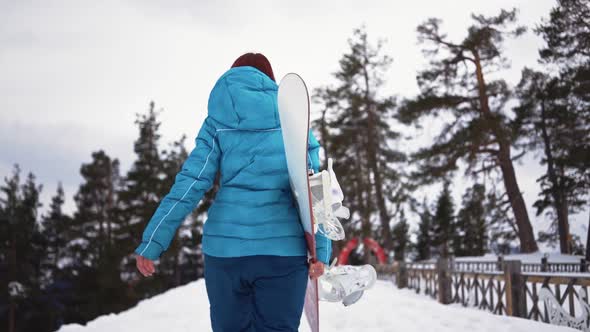 Girl Walks with Snowboard in Her Hands in Snow
