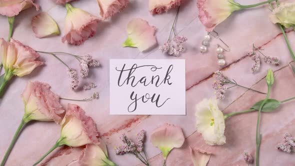 THANK YOU card on a marble table near pink flowers top view zoom in