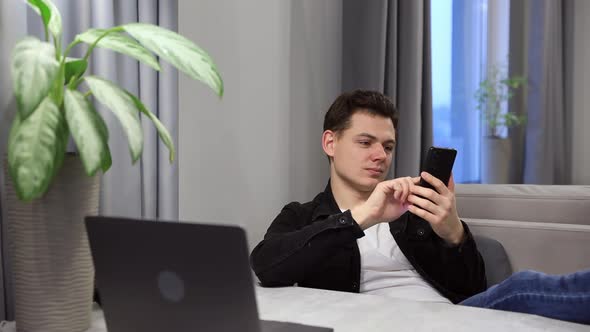 Young Man Holding Smart Phone Arrange Delivery and Resting at Studio Apartment