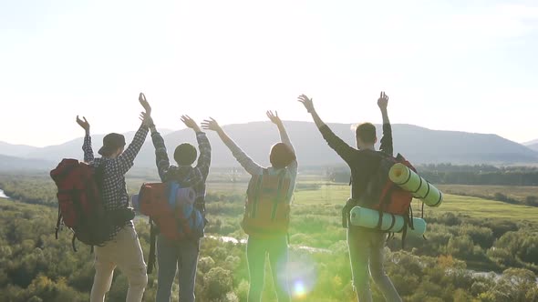 Two Couples of Young Travelers Waving at the Top of a Mountain