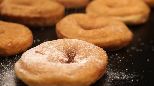 A sugar powder falls on a doughnuts on the black desk