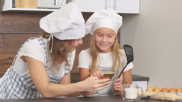 Beautiful Mother and Daughter Look at Each Other with Love Going To Bake in Kitchen