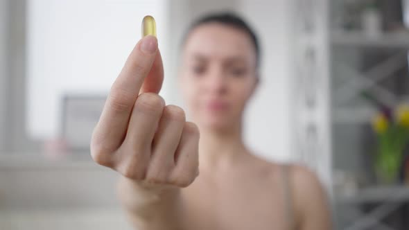 Closeup Yellow Vitamin D Omega3 Pill in Female Caucasian Hand with Blurred Slim Confident Woman at