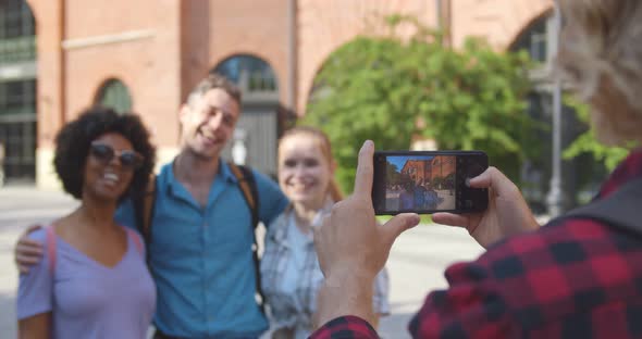 Over Shoulder View of Young Man Taking Photo of Happy Friends on Smartphone Traveling Together