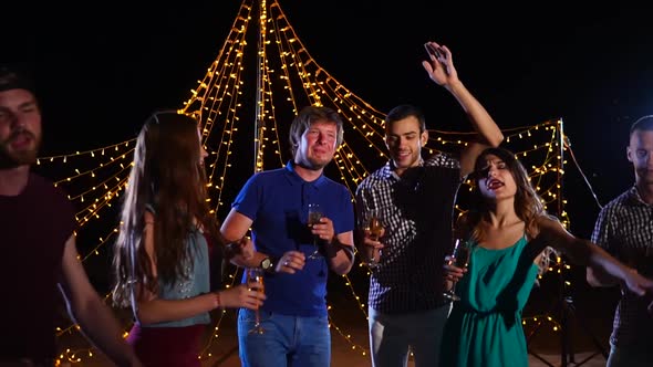 Young Friends with Glasses of Alcohol in Hand Actively Dance at a Beach Disco