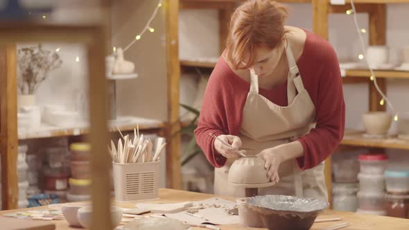 Caucasian Female Potter Shaping Bottom of Clay Bowl with Wire Tool