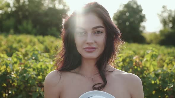 Amazing Girl Smiling Lightly at Camera and Putting on Hat Among Plantation