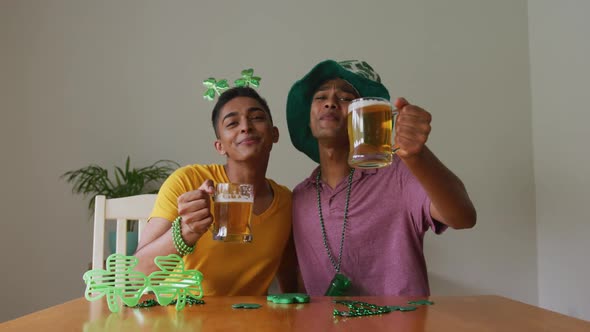 Mixed race gay male couple making st patrick's day video call raising glasses wearing costumes