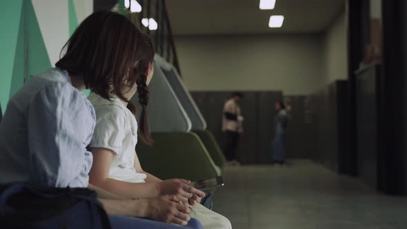 Two Schoolgirls Smile Holding Smart Pad in School Hallway