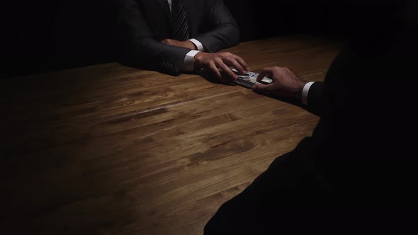 Businessman giving money to his partner on the table in the dark