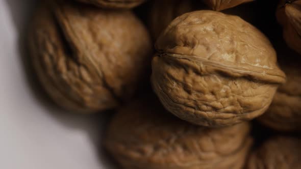 Cinematic, rotating shot of walnuts in their shells on a white surface 