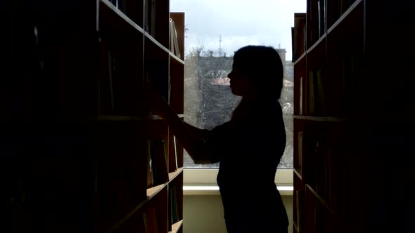 Silhouette of Young Student Reading a Book in a Library