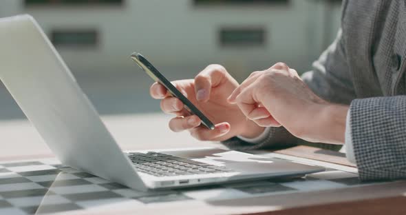 Closeup of Male Hands Who is Working on Laptop and Scrolling the Smartphone