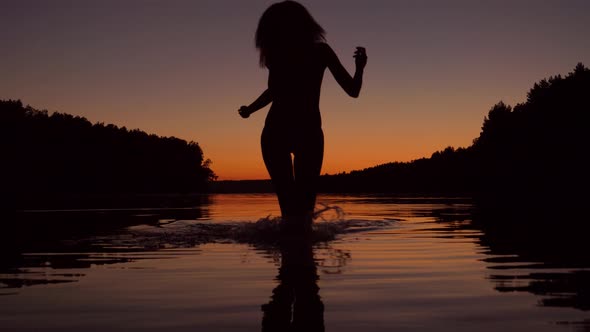 Silhouette Of A Woman Running Knee Deep In The Water Of The Lake At Sunset