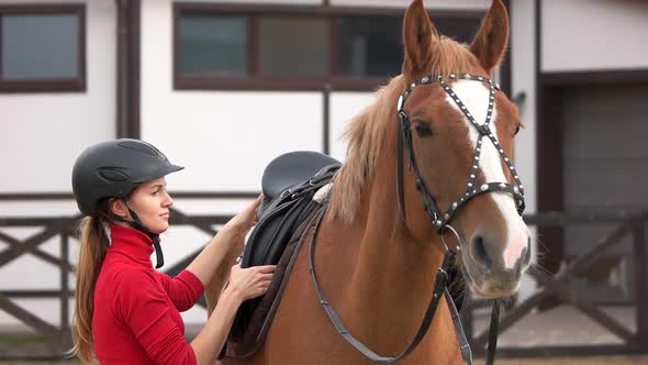 Pretty Girl Preparing Saddle for Riding Horse