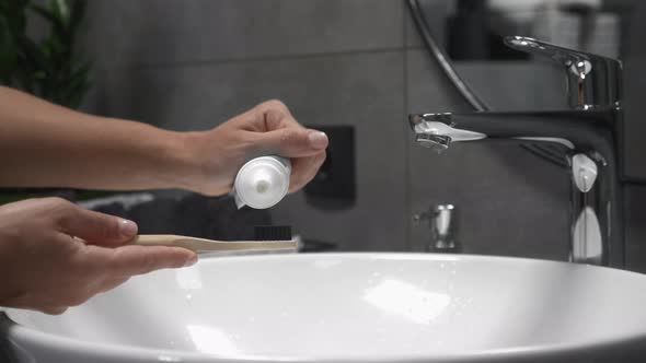 Female in bathroom puts toothpaste on toothbrush, prepared to brush teeth.