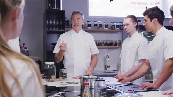 Professional Caucasian male chef in a restaurant kitchen teaching a group of trainee chefs