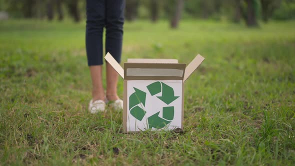 Box with Recycling Sign on Park Lawn with Teen Legs Passing As Unrecognizable Ecoactivists Putting