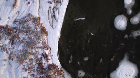 Birds eye view of frozen river covered by white snow. The point of view go forward to keep showing o