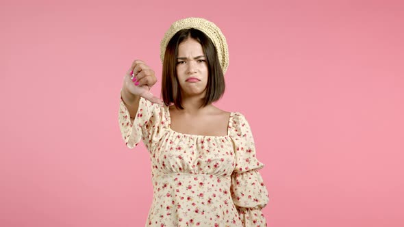 Young Asian Girl Standing on Pink Studio Background Expressing Discontent and Showing Thumb Down