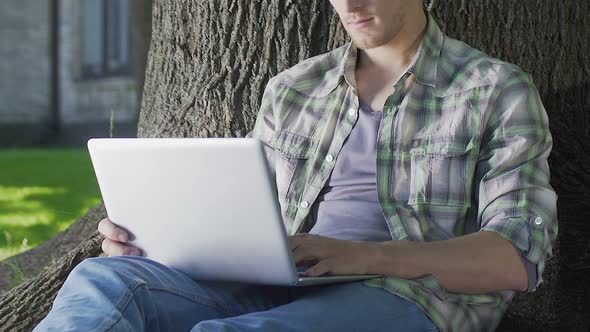 Young Man Sitting Under Tree Using Laptop, University Student Working on Project