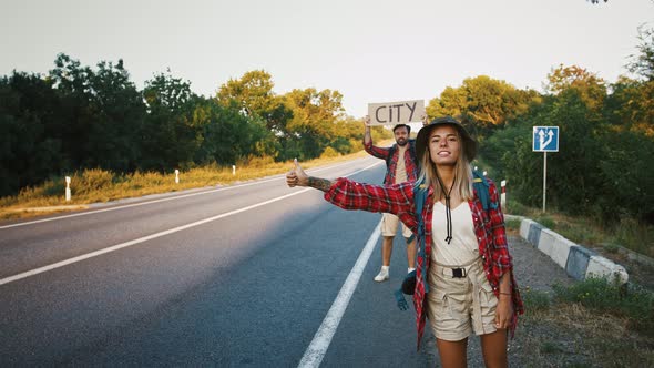 Young Man and Woman Trying to Stop Car on Road Holding Placard with Text City