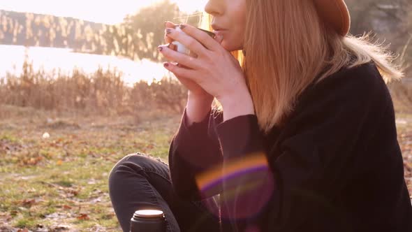 Slow Motion Caucasian Blonde Woman with Beige Hat in Black Sweater Drinks Hot Tea From Thermos in