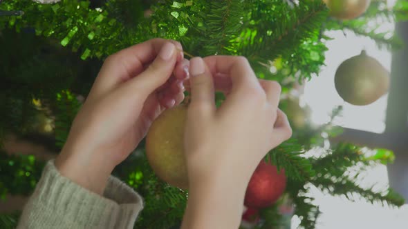 Woman's Hands Decorating on Christmas Tree with Yellow Ball.