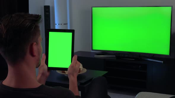 A Man, the Back of His Head Turned To the Camera, Holds a Tablet and Watches a TV - Green Screen