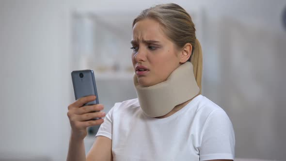 Woman in Foam Cervical Collar Reading Message on Cellphone, Feeling Pain in Neck