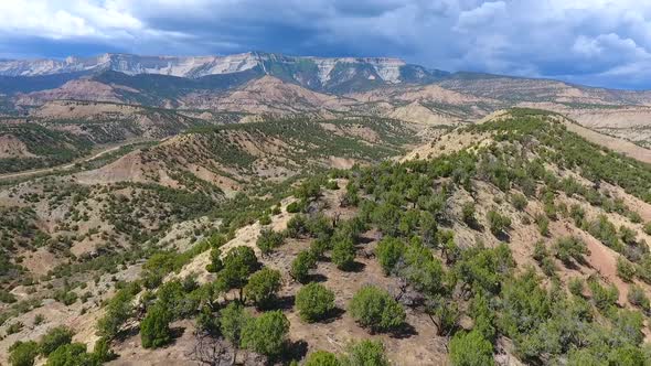 Aerial Over Top of Sandy Desert Mountains with Mountain Range and Storm in Distance