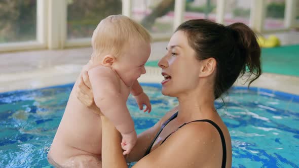 Happy Mother in Red Swimming Suit with Baby Son Surfing Water with Fun in Swimming Pool