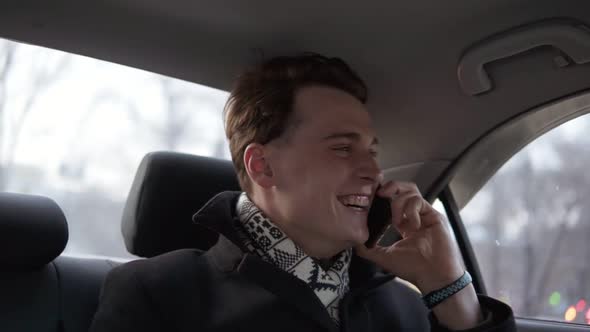 Attractive Sexy Guy in Black Stylish Coat is Smiling While Talking to Someone on the Phone in a Car