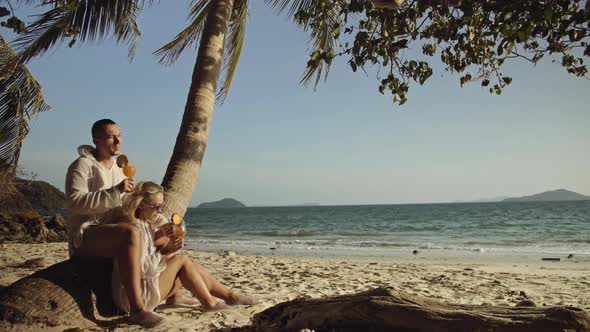 Loving Couple in White Dress and Sunglasses Near Palm Tree Relax and Drinking Cocktail