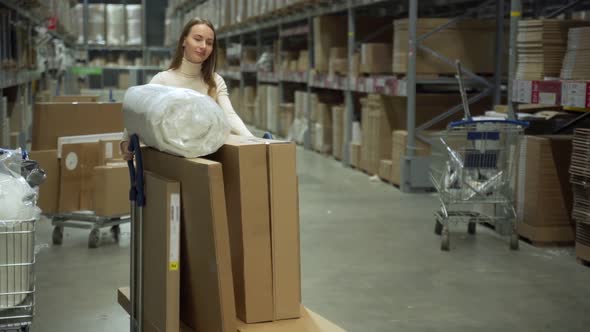 In the Warehouse Storage a Woman Drives a Shopping Cart and Selects Goods