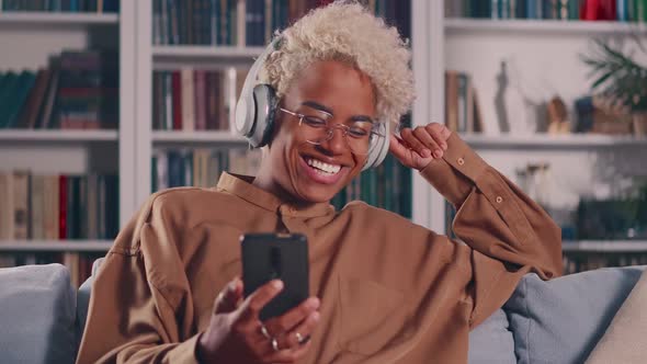 Female Wear Headphones Sit on Sofa with Smart Phone Laughing During Video Call