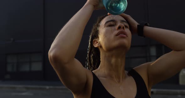 Front view of young African American woman pouring water on her head in the city 4k