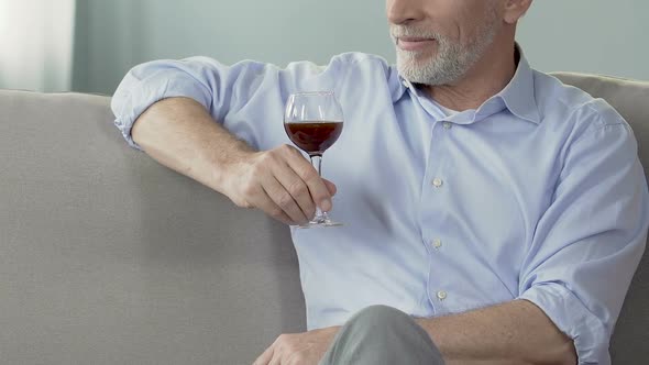 Elderly man sitting on sofa with glass of wine, enjoying moment, private winery