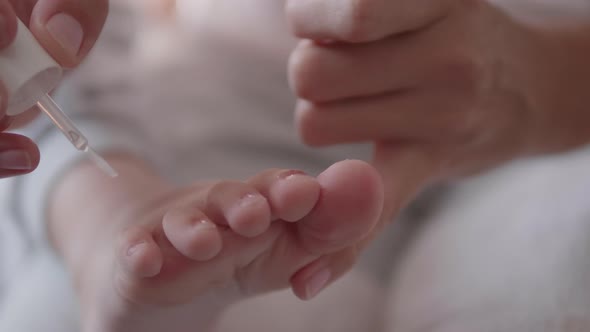 Mother Massages Nails on Her Child's Toes with Body Oil After Pedicure