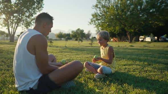 Family Leisure and People Concept  Happy Father Juggling Apples and Son Learning