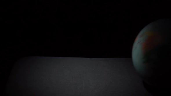 Geographic Globe Rolls on a Black Surface in Slowmo